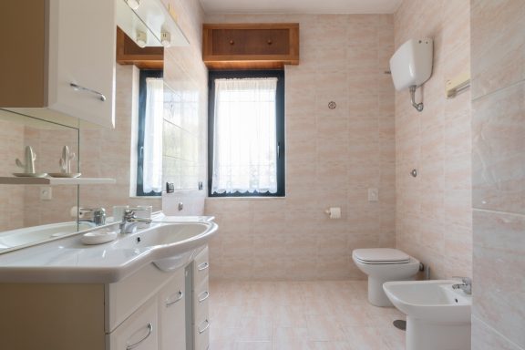 Bagno moderno con lavandino, wc e bidet, illuminato da finestre. Pareti chiare e piastrelle.