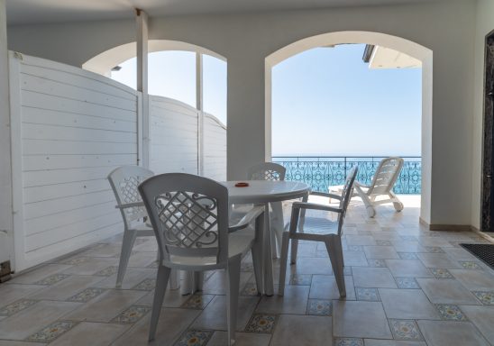 Terrazza con tavolo e sedie, vista sul mare e archi che incorniciano il paesaggio.