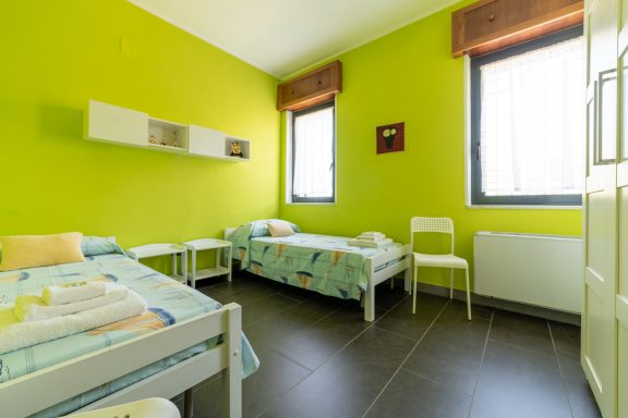 Camera captures a bright green bedroom with two beds and minimalist decor.