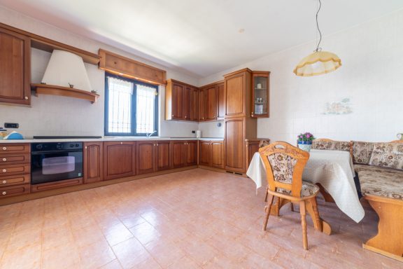 Cucina moderna con armadietti in legno, tavolo, sedie e finestra luminosa.